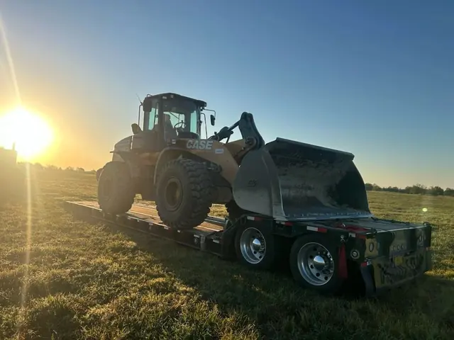 A CASE wheel loader secured on a lowboy trailer at sunrise